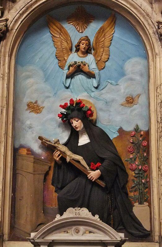 Statue of Saint Rita holding a cross with an angel blessing her with roses